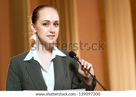 Portrait of a business woman holding a microphone and looks to the camera