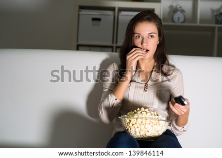 Young woman watching TV on the couch, eating popcorn