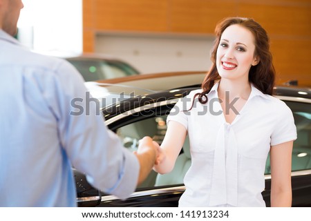 Woman shaking hands with car salesman, buying a new car