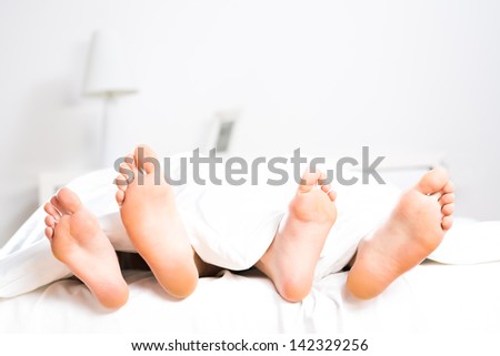 women\'s and men\'s feet sticking out from under the covers