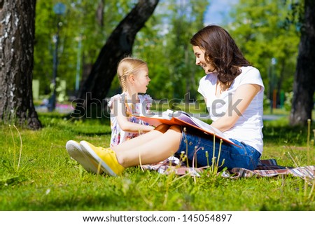 girl with the teacher reading a book together in the summer park