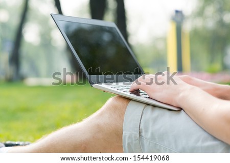 young man in the park sitting on the grass with a laptop, close-up hands and laptop