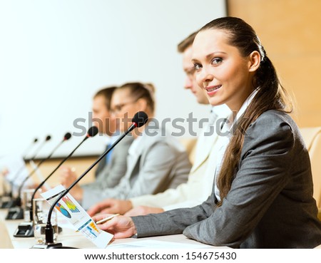 group of business people sitting at the tables at the presentation, woman looking at the camera