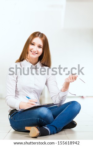 Portrait of an attractive woman sitting on the floor cross-legged and holds the tablet for notes