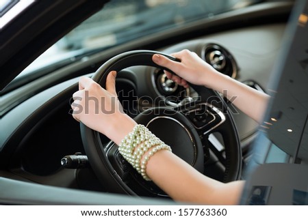 woman\'s hands holding on to the wheel of a new car in the showroom