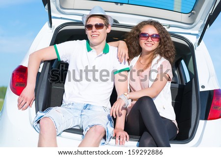 young couple sitting in the open trunk of a new car, a summer road trip