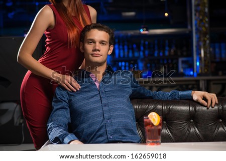 Portrait of a successful man in a nightclub, sitting on the couch, next to a woman in a red dress