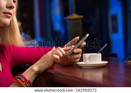 close-up of female hands holding a cell phone, sitting at the bar, next to a cup of coffee