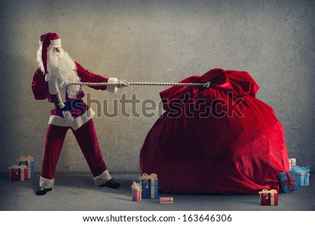 Santa Claus pulls a huge bag of gifts lying around boxes with gifts