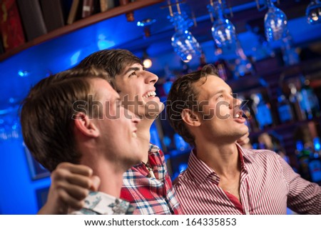 Three men stand in a row embracing smile and look in front of you, sports fans