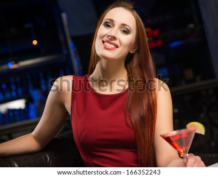 Portrait of an attractive woman in a nightclub, sitting on the couch with a drink