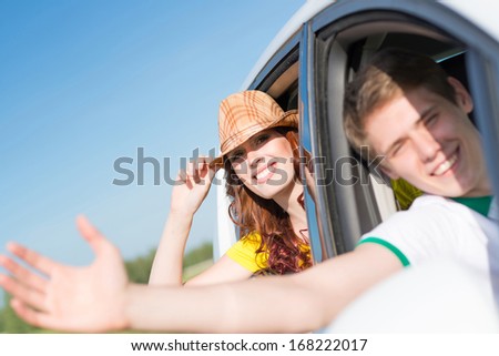 Young woman looking out of car window, holds the hand hat and smiling