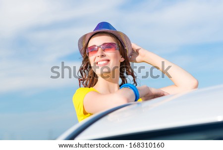 young woman got out of the car window, holds the hand hat and laughing