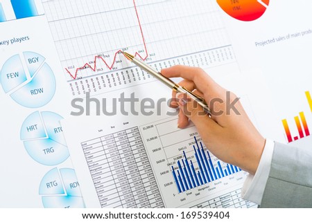 female hand pointing pen on financial charts, paper work in the office