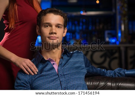 Portrait of a successful man in a nightclub, sitting on the couch, next to a woman in a red dress