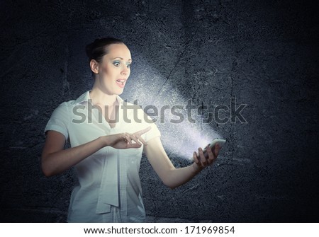 young attractive woman holding a cell phone in a dark room at her glow from the monitor