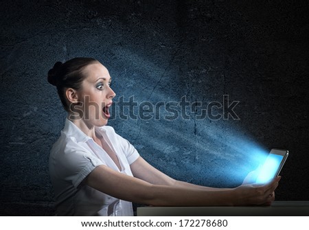 young attractive woman holding a tablet in a dark room at her glow from the monitor