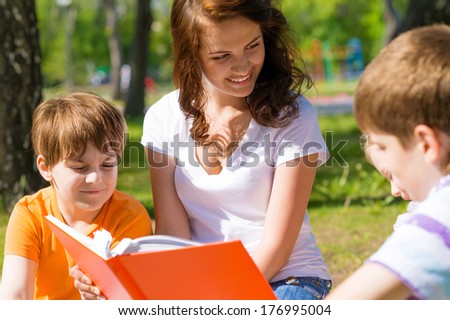 children and teacher reading book together in the summer park