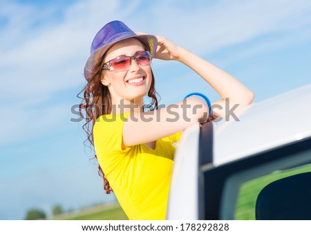 young woman got out of the car window, holds the hand hat and laughing