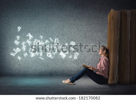 image of a young woman reading a book sitting near a big book