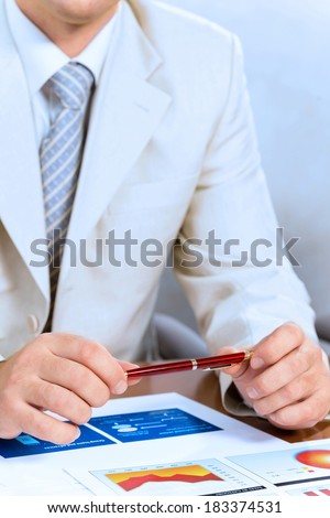 businessman holding a pen in hand, in front of him laid paper business financial charts