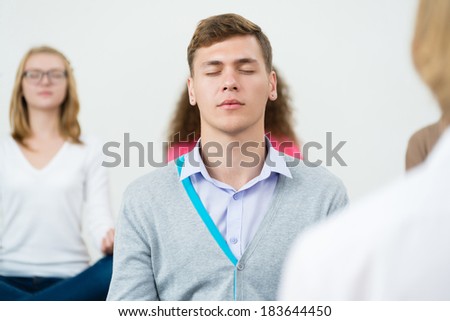 young man, meditating with closed eyes, group meditation