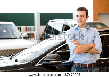 man standing near a car with his arms crossed, car showroom