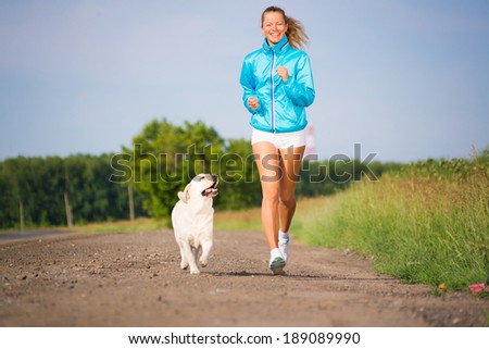 young woman with labrador running on a country road, outdoor training