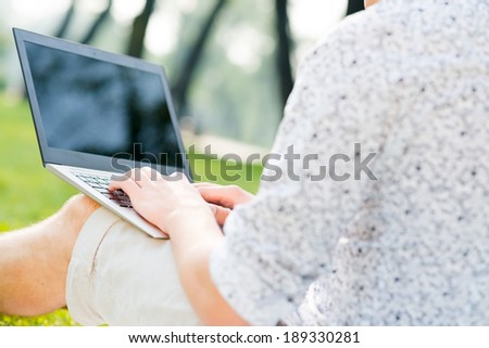 young man in the park sitting on the grass with a laptop, close-up hands and laptop