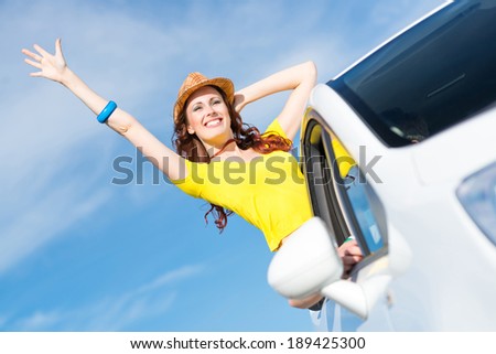 young woman got out of the car window, holds the hand hat, waving his hand and laughing