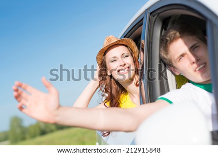 Young woman looking out of car window, holds the hand hat and smiling