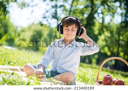 Young joyful boy in summer park wearing headphones
