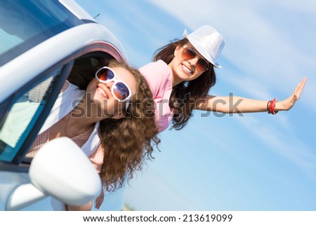 young woman got out of the car window, holds the hand hat, waving his hand and laughing
