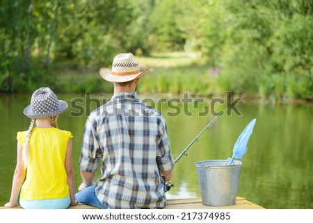 Back view of father and daughter sitting on bridge and fishing