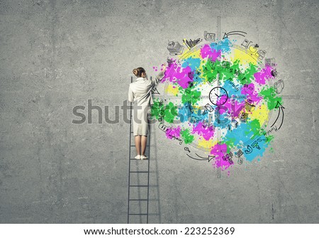 Back view of businesswoman standing on ladder and drawing on wall