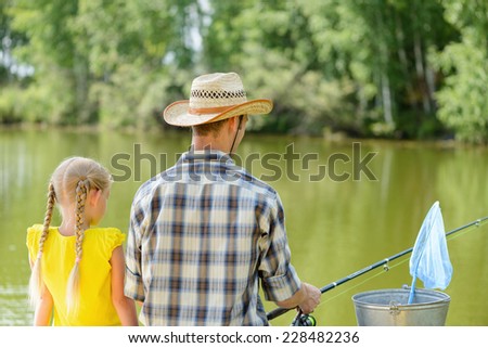 Back view of father and daughter sitting on bridge and fishing
