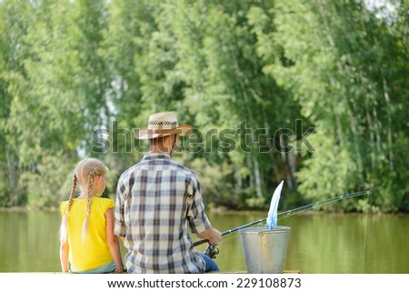 Back view of father and daughter sitting on pier and fishing