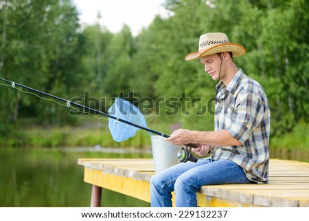 Handsome young man sitting on pier with rod
