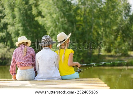 Back view of three children sitting on wooden pier with rod