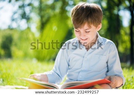 Little adorable boy in sitting park with book in hands