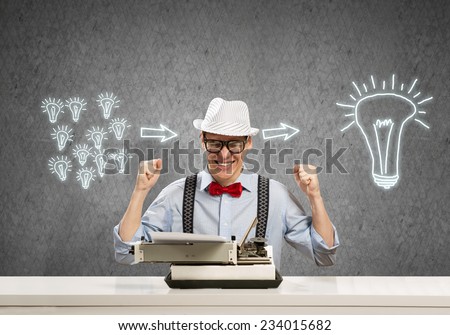 Young guy writer in hat and glasses using typing machine
