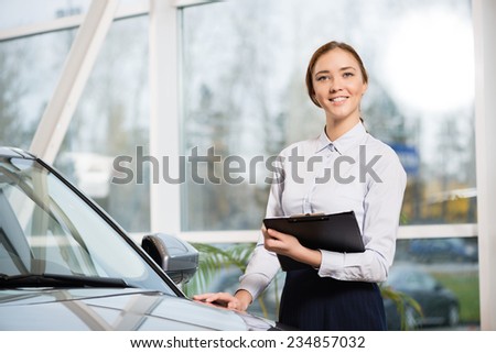 Young woman consultant in show room standing near car