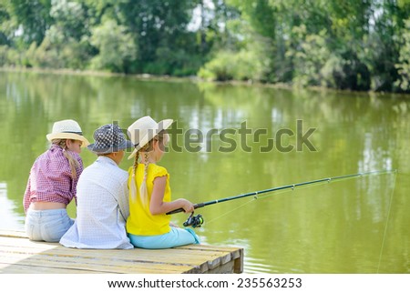 Back view of three children sitting on wooden pier with rod