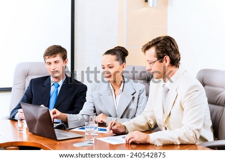 Business people talking, sitting at the table, watching the presentation on a laptop