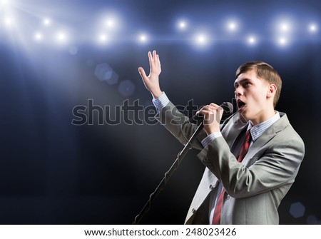 Young handsome businessman sining on stage in microphone