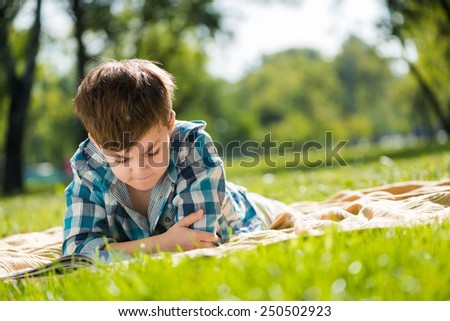 Cute boy in summer park lying on blanket and reading book