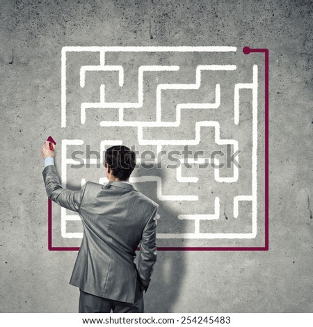 Back view of businessman drawing labyrinth on wall