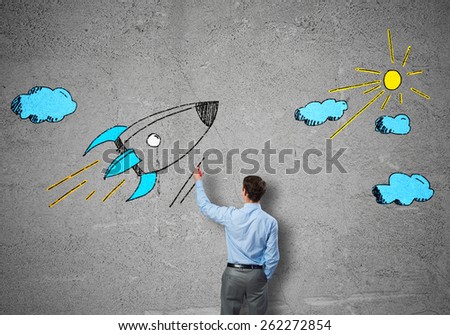 Rear view of businessman drawing rocket on wall