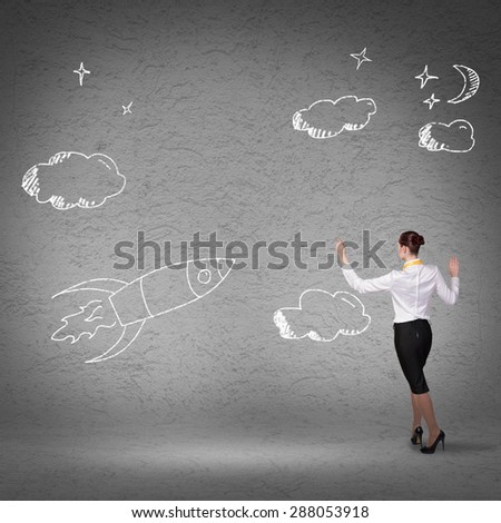 Rear view of businesswoman drawing rocket on wall