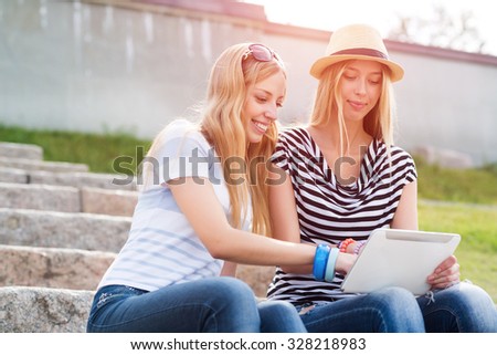 Two young female friends sitting on steps and using tablet pc